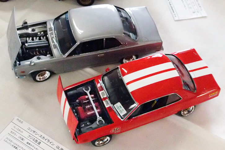 フジミ製1/24「日産スカイライン・ハードトップ2000GT-R」をベースとする2台の空想ハコスカ。奥は製作者が実車でいつか実現したい仕様だそうで、“R”ではない2000GTのL型エンジンをLYヘッド（日産ワークスがS30Zに使っていたクロスフローのヘッド）などでチューン、見えないが内装もマッハのステアリングホイールやロンサムカーボーイ（カーコンポ）でキメている。手前は切り詰めたノーズに直4 DOHC 16バルブのFJ20型エンジンを積んだ「ハードトップ1800GL改」。ハコスカ世代に「2000RS」があったら、というモデルだが、個人的にはこちらのほうに興味がある。