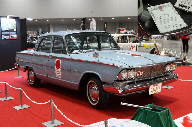 企画展示車両の1964年「プリンス・グロリア デラックス」は、東京オリンピックの際に日本オリンピック委員会（JOC）に公用車として提供されたヒストリーを持つ個体。カタログにはないソリッドカラーのライトブルーで塗られており、オリンピック終了後に販売された際の証明書（写真右上）も残されている。手前に置かれた聖火リレー用のトーチは、当時スペアとして用意された未使用のホンモノとのこと。