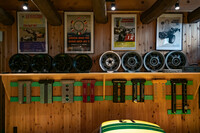 ガレージに彩りを添える定番アイテム。古き良き時代のレースのポスターが泣かせる。右端は画家に依頼したクーパー・マセラティをモチーフにした作品。ホイールの置かれた棚の下には、ロータス・エラン、トヨタ2000GTなどのさまざまなカムカバーがずらりと並ぶ。