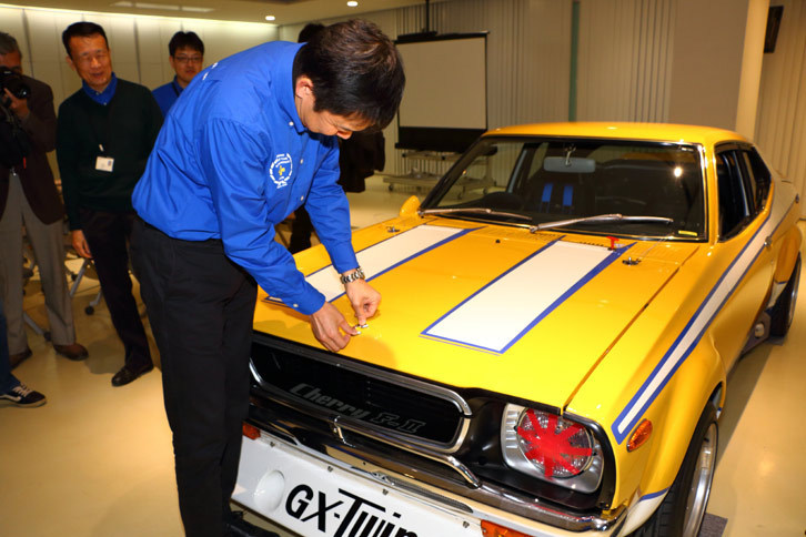 レストアの仕上げとして、ボンネットにエンブレムを装着する日産名車再生クラブの木賀新一代表。