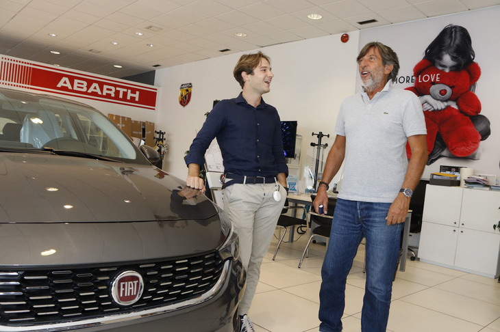 ふだんは4人の先輩とともに席を並べる。そのうちのひとりであるフランチェスコさんと。傍らにある展示車両は「フィアット・ティーポ」。