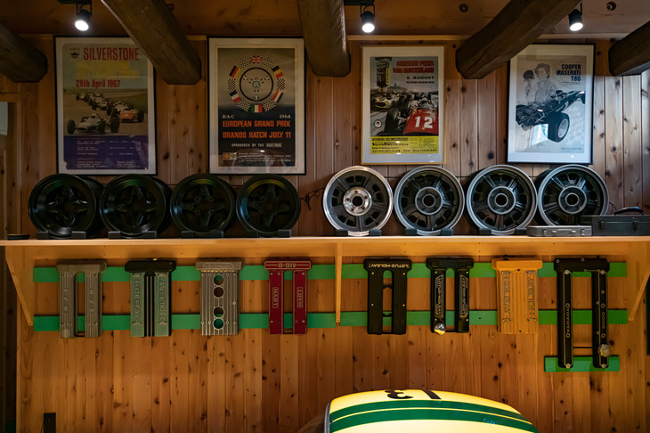 ガレージに彩りを添える定番アイテム。古き良き時代のレースのポスターが泣かせる。右端は画家に依頼したクーパー・マセラティをモチーフにした作品。ホイールの置かれた棚の下には、ロータス・エラン、トヨタ2000GTなどのさまざまなカムカバーがずらりと並ぶ。