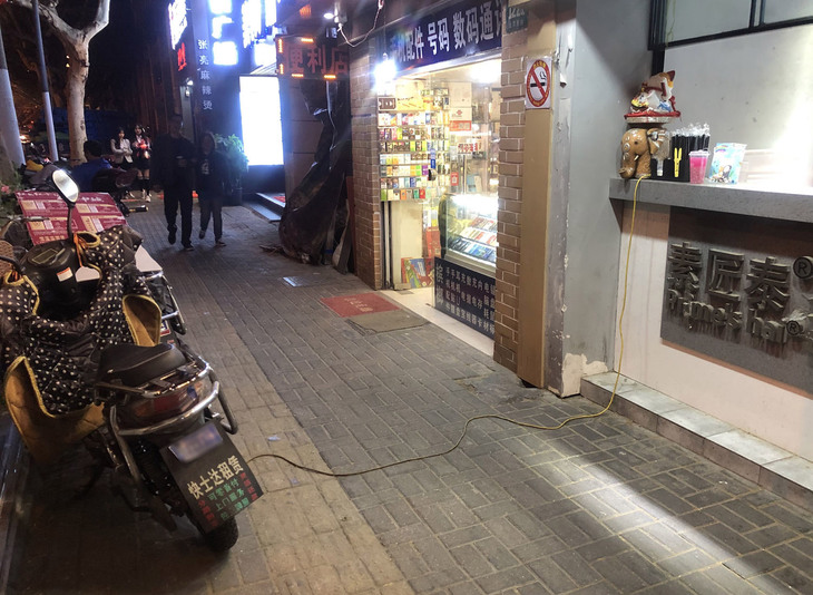 上海市街の北京西路で。店頭から伸びたコードで電動スクーターを充電中。