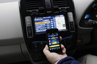 「日産リーフ」の各種情報画面。写真奥のセンターコンソールに表示されているのは「充電ポイントの検索画面」で、手前のスマートフォンに見られるのは「現在の充電状況」。