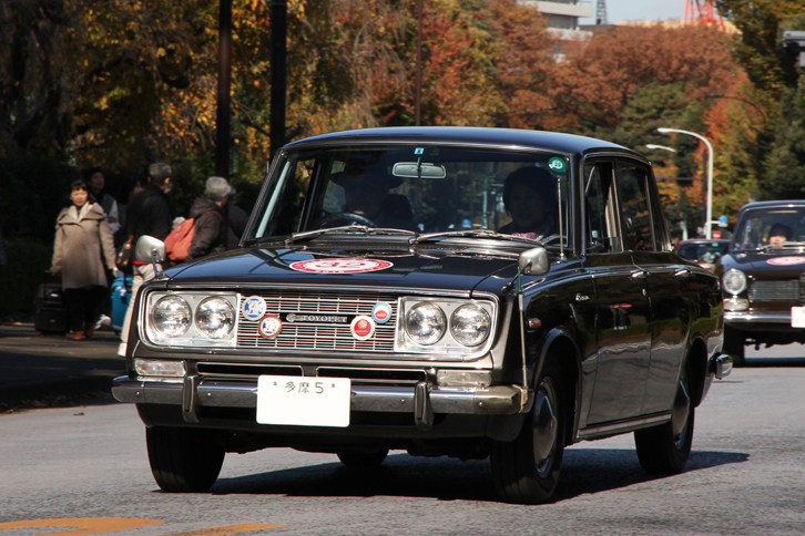「多摩5」のシングルナンバー付きの1965年「トヨペット・コロナ デラックス」。1964年にデビューした3代目コロナの初期型で、新車からのワンオーナー車。オーナーは参加者代表として、オープニングセレモニーでスピーチを行った。