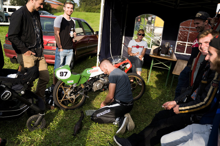 タイム計測を終えた土曜日の夕方、翌日の走行に備えてマシンの整備を行うライダー。それを囲んだ仲間たちは話をしたりビールを飲んだり。ゆっくりとした時間が流れる。