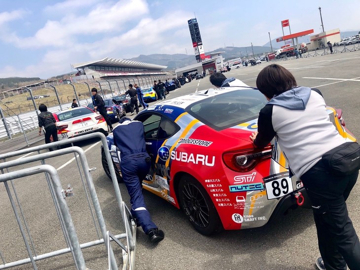 予選日の朝、まずドライバーはメディカルチェック。車両の準備は公式車検から始まります。これは公式車検に並ぶ89号車の写真。台数が多いので毎回大行列です。89号車の担当メカニックさんたちが少しずつ押しながら、車検場へと進んでいきます。マネージャーの麻衣子さん（写真手前）も押してくれました！