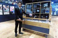 貴重な自動車切手の展示を紹介する学芸員の川島信行氏。世界初の自動車切手は1901年にアメリカで発行されたもので、当時メジャーな存在だった電気自動車が描かれていた。