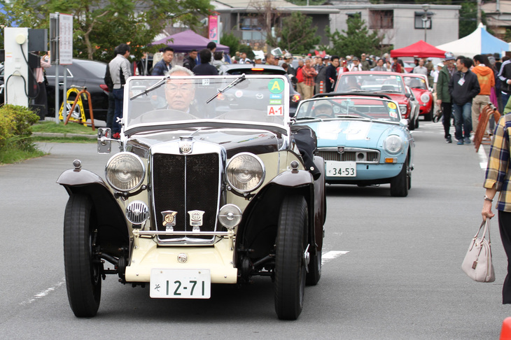 1935年「MG NA」を先頭に、芝生広場から「ロングビーチスラローム」と題されたパイロンスラロームのコースへと移動する参加車両。