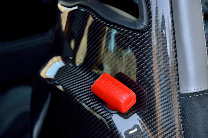カーボンシェルを持つSabelt製スポーツシート（前席）の背後には、まるでキルスイッチのような赤いレバーが。後席への乗り込みに際して、前席の背もたれを前方に倒すためのものである。