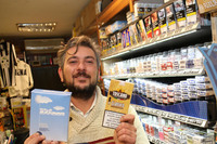 シエナのタバコ店で。店主が手にする葉巻パッケージの警告は、EU基準よりやや小さめ。だが「喫煙は死に至ります」の文字とともに、禁煙相談の電話番号が記されている。後方の箱には患部や、二次喫煙から守るべき幼い子どもの写真が。