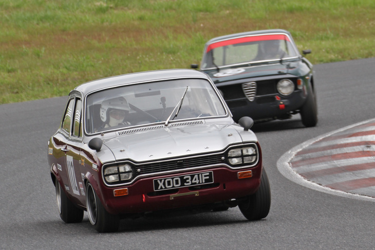 1950～69年の量産サルーンによる10周のスプリントレースであるティントップ・カップ決勝で、終始激しいトップ争いを演じた1968年「フォード・エスコート ツインカム Mk1」と1967年「アルファ・ロメオ・ジュリア スプリントGTヴェローチェ」。予選2位のエスコートがポールポジションのアルファを1周目で逆転、そのままゴールを迎えた。