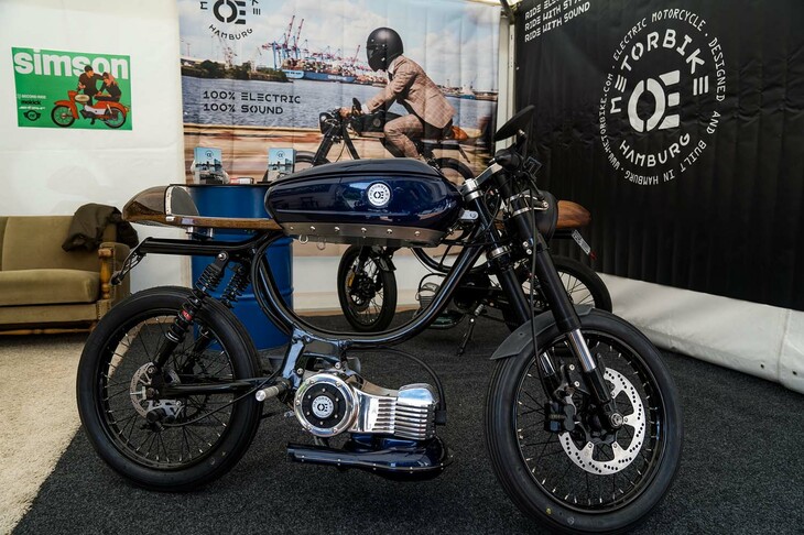 ドイツ・ハンブルグで活動するMETORBIKE（メトロバイク）の電動バイク。オーストリアのバイクブランド、PUCH（プフ）の小排気量車用フレームに、モーターとバッテリーを搭載している。革巻きのハンドルグリップや木製のシートカウルなど、クラシックとモダンを掛け合わせたスタイルが特徴だ。なによりもユニークなのは、アクセルワークと連携したサウンドシステムを採用していること。V8などの四輪車用エンジンの排気音、並列4気筒エンジンや2ストロークエンジンを搭載したスポーツバイクの排気音、さらには映画「スター・ウォーズ」に登場する「タイファイター」の飛行音に似たデジタルサウンドまで、全8種類の走行音をセット。エンジンの形をしたモーターの下に見える、マフラーのような部品がスピーカーだ。地面に向けて音を発することで、ライダーや道を歩く人々に、よりクリアに走行音を聞かせられるという。もちろんスピーカーは防水仕様。