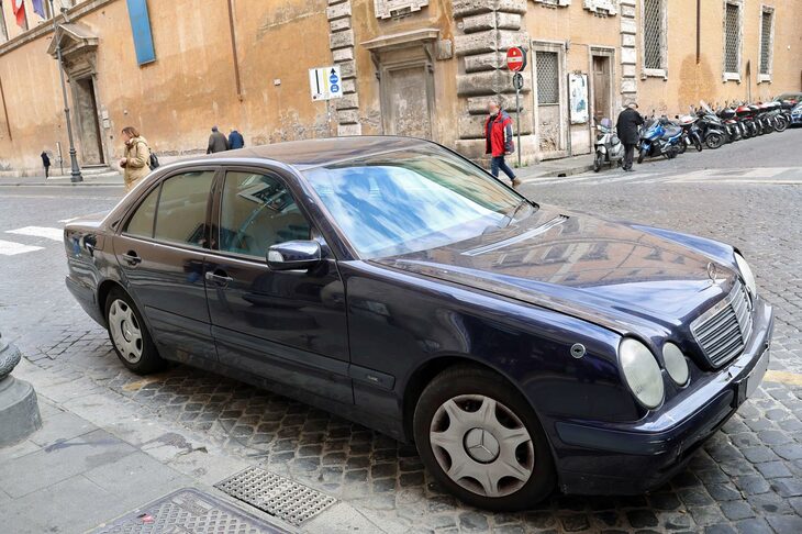 外交官ナンバーの「メルセデス・ベンツEクラス」（W210）。フロントフェンダーには国旗ポール立てがある。車齢は最低でも21年。こういう節約志向の国に住みたいものだ。