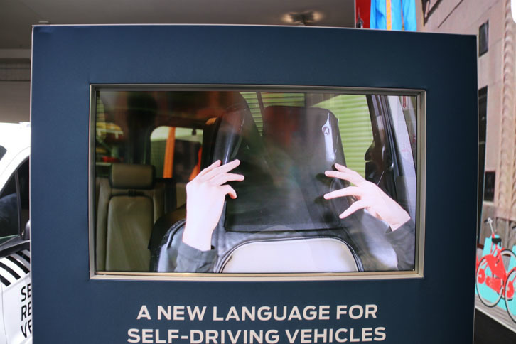 フォードのブースにて。ヘッドレスト風の半透明マスクをかぶり、人が運転していないように見せかける“なんちゃって自動運転”の展示。自動運転に対する歩行者の反応や、彼らとの関わり方を探る研究である。